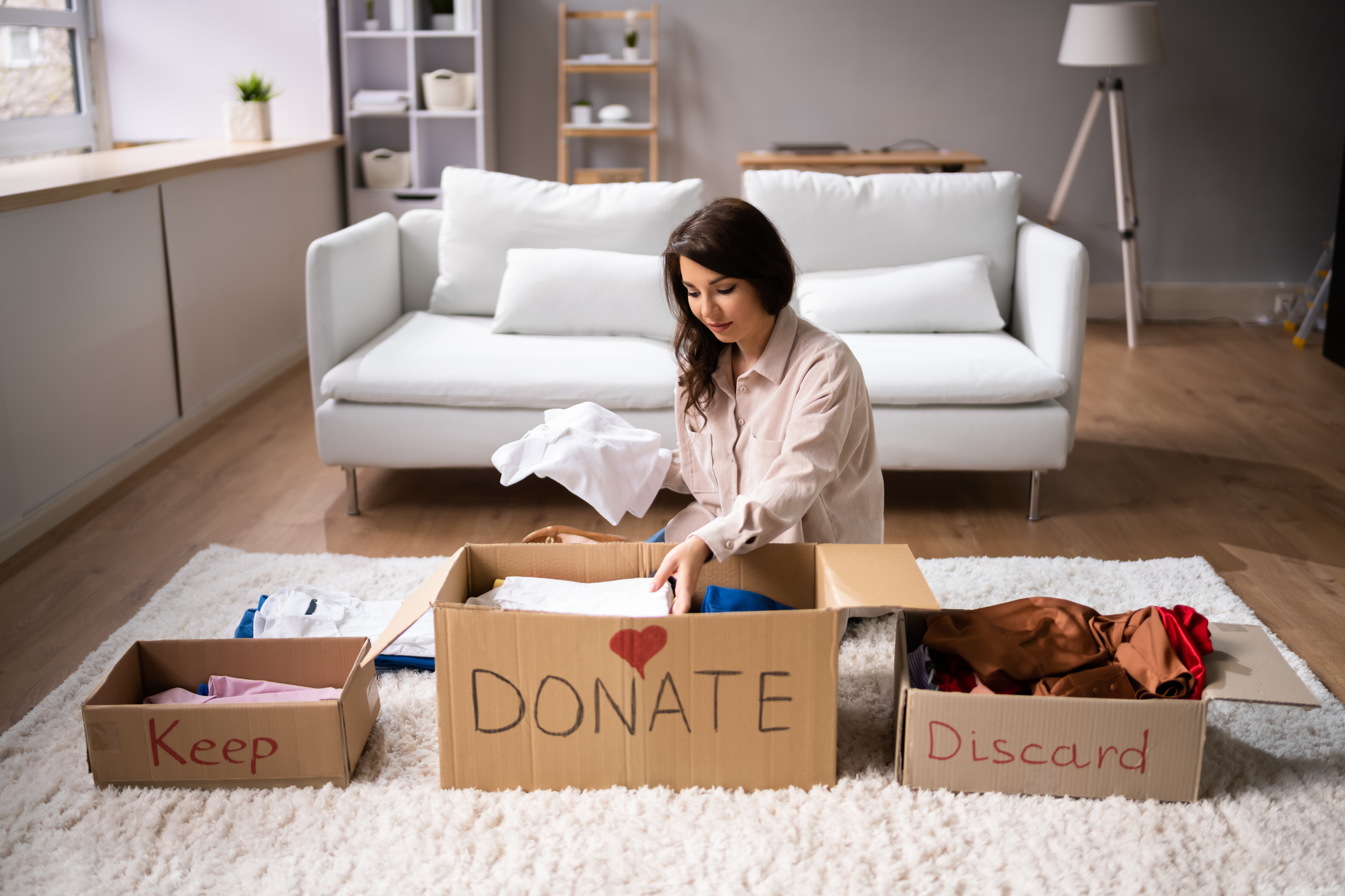 woman organizing items into three boxes to keep, donate, or discard