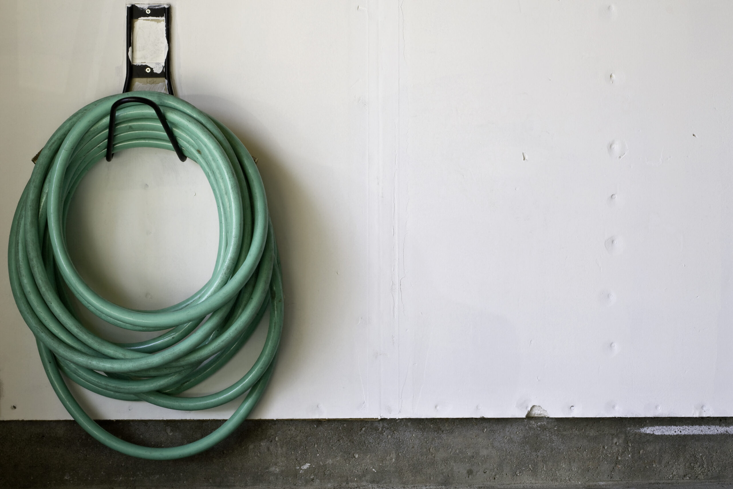 A green garden hose hanging on the garage wall