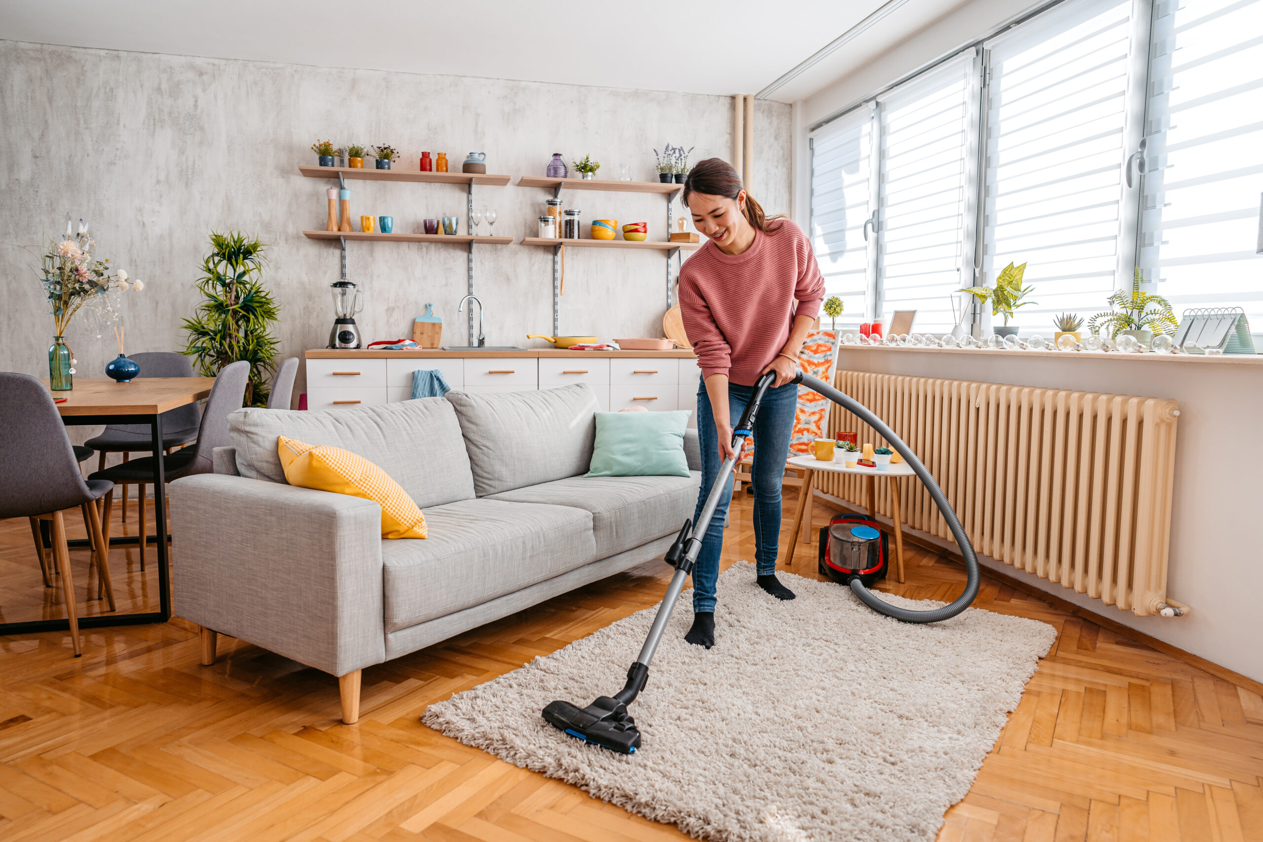 Young woman vacuuming rug at home