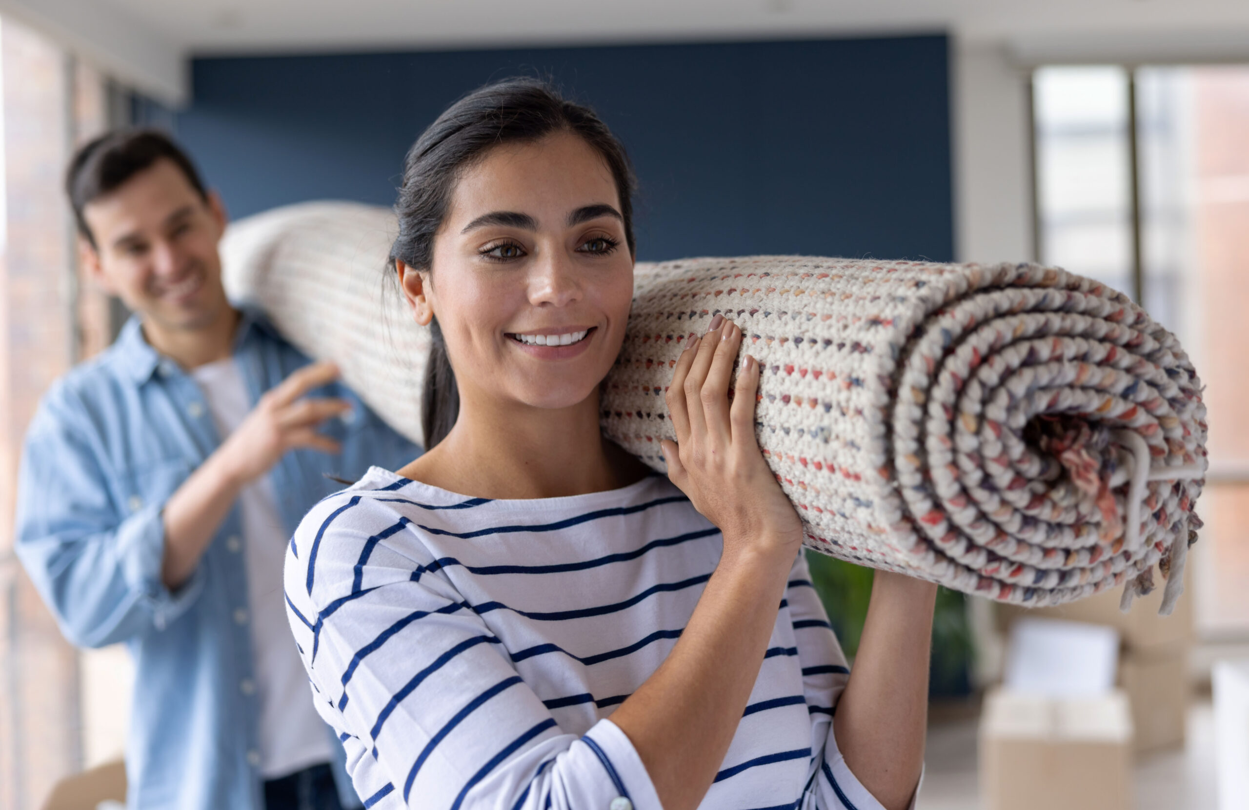 Young couple moving house and carrying a rolled carpet 