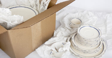 dishes being wrapped in tissue paper and packed in a cardboard box to show how to pack china for moving