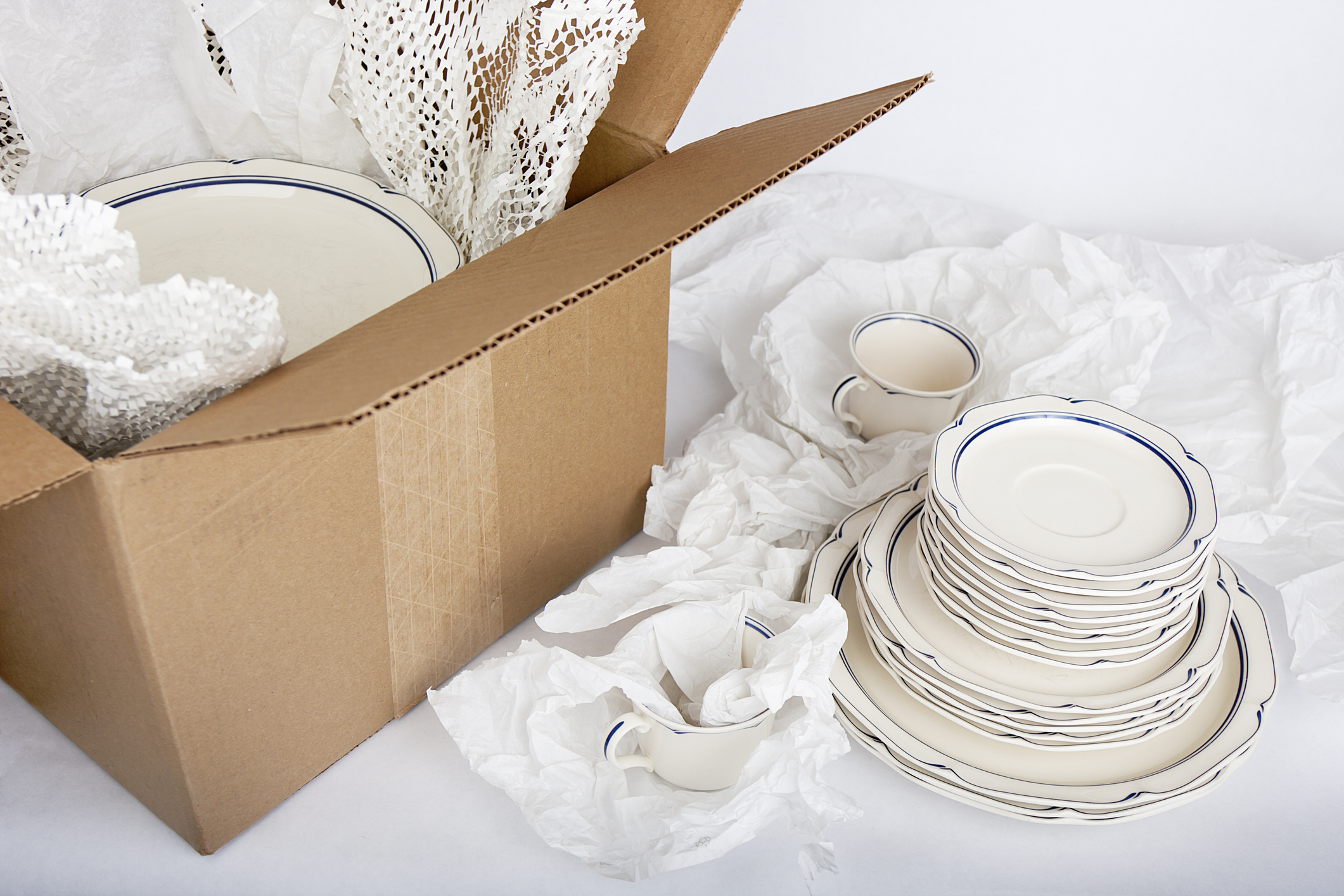 dishes being wrapped in tissue paper and packed in a cardboard box to show how to pack china for moving
