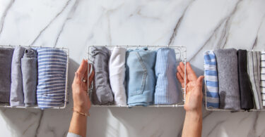 how to marie kondo your closet with neatly folded clothes and pyjamas in the metal mesh organizer basket on white marble table.