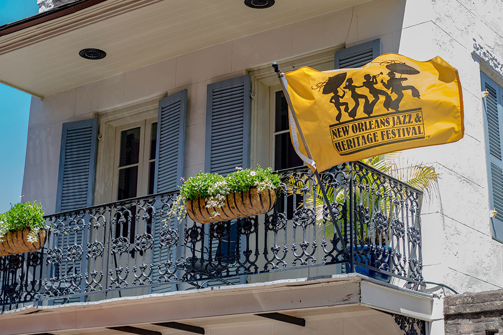 Moving to New Orleans - Jazz Festival flag flying from an older home with plants on a blue porch