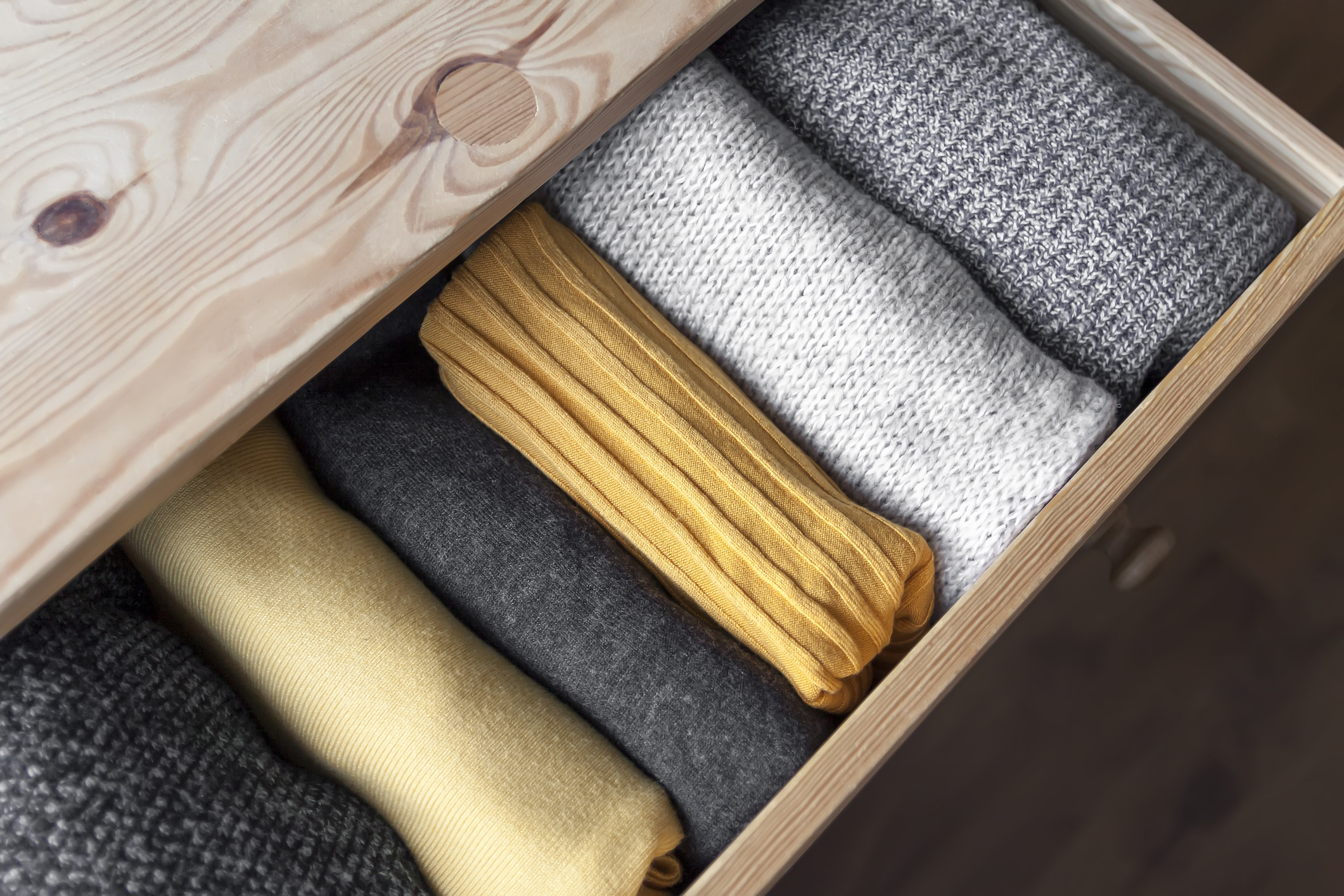 Open wooden dresser drawer with warm knitted sweaters stored inside