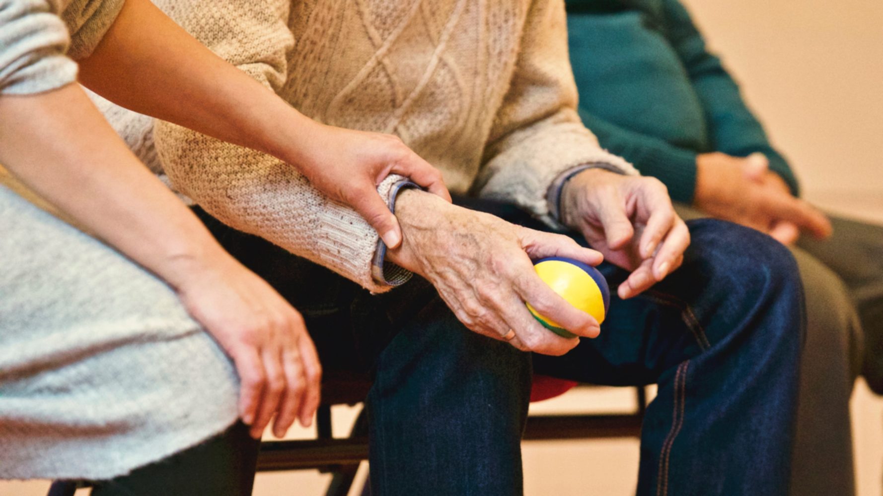 Image of senior's hand using a stress ball while receiving emotional support from a relative