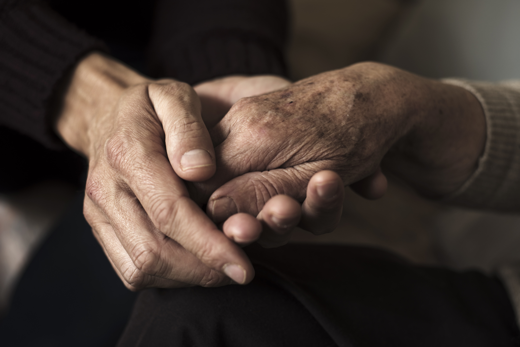 moving in with elderly parents - closeup of a young caucasian man holding the hand of an old caucasian woman with affection