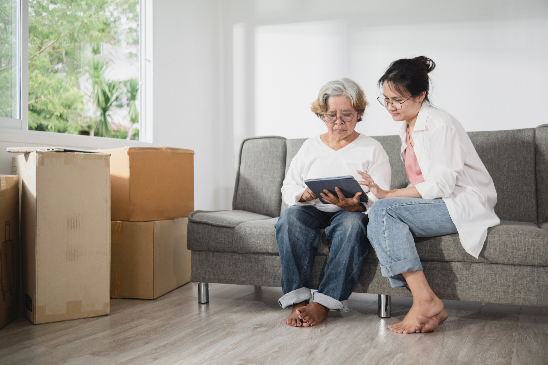 moving in with elderly parents - Asian elderly woman and daughter sitting in living room with moving boxes