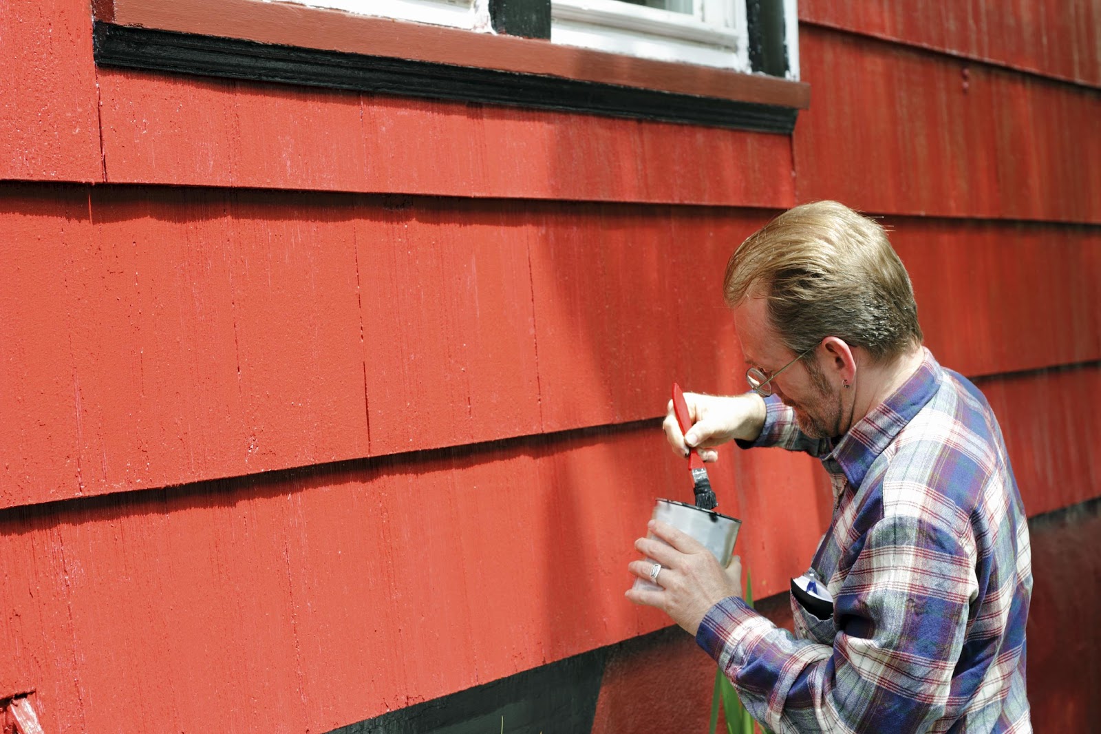 Male homeowner painting red exterior of home to increase curb appeal